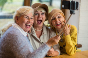 Women taking selfie at table. Three senior ladies laughing. Friendship is priceless.
