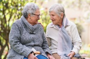 Two elderly women sitting on bench in park smiling happy life long friends enjoying retirement