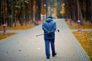 Elderly man walking with walking cane in hand behind his back. Old man with cane enjoying walk in autumn city park. Senior man walk alone